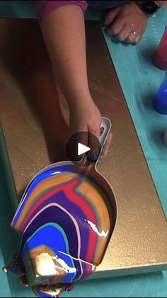 a person is painting a colorful vase on a table with gold foil and blue paint