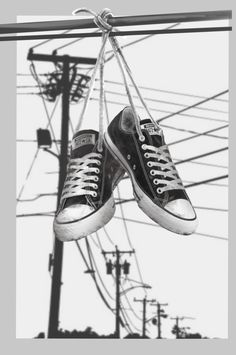 black and white photograph of tennis shoes hanging from power lines with wires in the background