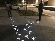 two men are walking down the sidewalk at night with their shadows projected on the pavement