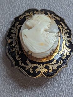 "Antique Shell Cameo & Black Enamel Brooch Pin HALLMARKS Unmarked. MEASUREMENTS 1 3/8\" x 1 5/8\".               MATERIALS Shell, Black Enamel, Gold Gilt. CONDITION In very good condition with minimal wear on gold gilt, please use all pictures as part of item's description. Turn of the Century Edwardian era Mourning Cameo brooch featuring carved shell center of classic Roman or Grecian lady in profile prong set in Black Enamel frame with ornate Gold Gilt designs. This is a very unique cameo. Cam Victorian Style Cameo Brooch For Weddings, Antique Cameo Brooches For Wedding, Victorian Cameo Brooch For Wedding, Antique Medallion Brooch For Wedding, Vintage Medallion Brooch For Wedding, Antique Baroque Brooches For Wedding, Ornate Medallion Brooch For Formal Occasions, Vintage Medallion Brooches For Wedding, Ornate Medallion Brooches For Formal Occasions