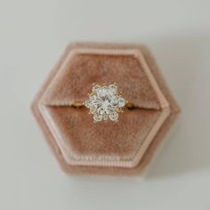 an engagement ring sits in a velvet box on top of a white surface with a hexagonal pattern around it