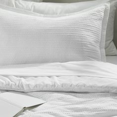 a bed with white sheets and pillows next to an open book on top of it