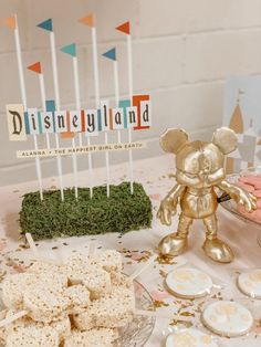 a table topped with lots of desserts next to a gold mickey mouse figurine