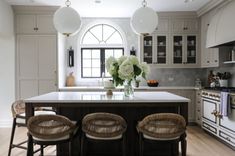 a kitchen with three stools at the center of the island and four lights hanging from the ceiling