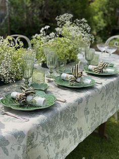 an outdoor table set with plates, glasses and flowers in vases on the table