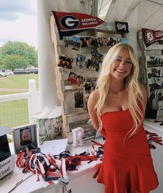 a woman in a red dress standing next to a table with pictures and ribbons on it