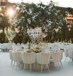 an outdoor wedding reception with chandeliers and white flowers on the table, surrounded by tall greenery