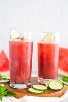 two glasses filled with watermelon and cucumber on top of a cutting board