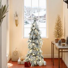 a white christmas tree sitting in front of a window next to a red tile floor