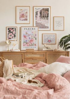 an unmade bed with pink linens and pictures on the wall