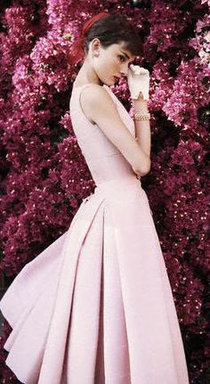 a woman in a pink dress is talking on her cell phone while standing next to purple flowers