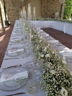 a long table is set with white flowers and place settings for an elegant dinner party