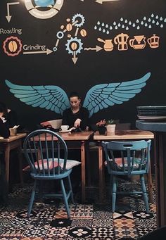 two people sitting at a table in front of a black wall with blue wings on it