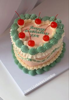 a green and white cake with cherries on it sitting on top of a table