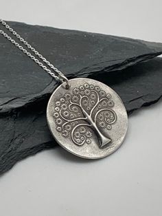 This unique tree of life handmade embossed round pendant has been entirely handmade using .999 fine silver. It has been cut from fine silver precious metal clay, textured, fired and oxidized. The pendant hangs from a sterling silver diamond cut cable chain. This fine silver pendant features an embossed tree of life on one side of the pendant and is reversible to a wood grain embossed pattern on the reverse side. Pendant size: approximately 1 x 1 inches Chain length: adjustable at 16 and 18 inche Antique Silver Stamped Jewelry For Gift, Silver Etched Nature-inspired Necklaces, Symbolic Silver Jewelry With Tree Of Life, Symbolic Silver Tree Of Life Jewelry, Antique Silver Etched Necklace As Gift, Nature-inspired Silver Etched Necklaces, Nature-inspired Stamped Sterling Silver Jewelry, Silver Engraved Nature-inspired Necklace, Symbolic Silver Necklace With Tree Of Life