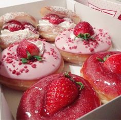 three donuts with strawberry toppings in a box on a table next to other doughnuts