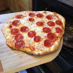 a pepperoni pizza sitting on top of a wooden cutting board in front of an oven