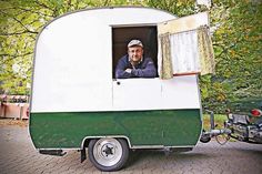 a man sitting in the window of a green and white camper trailer parked on a brick road