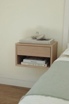 a nightstand with two books on top of it next to a white wall and a bed