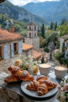 croissants and coffee are on a table overlooking the town's mountains