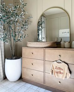 a dresser with a sweater on it next to a potted plant and mirror in the background