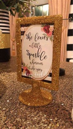 a sign that is sitting on top of a granite counter with gold glitter paint and flowers