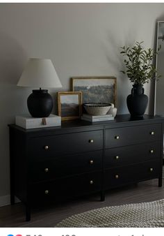 there is a black dresser with two vases on it and a lamp next to it