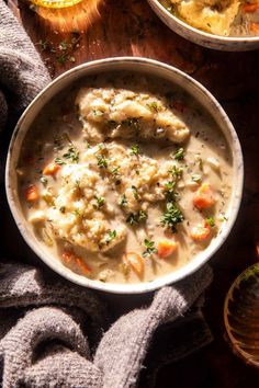 two bowls filled with chicken and dumplings on top of a wooden table next to bread