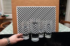 a hand is holding four glasses in front of a card on top of a table