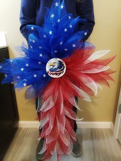 a person standing in front of a wall holding a red, white and blue wreath