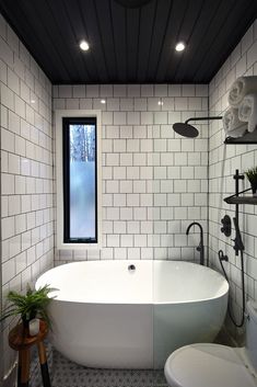 a white bath tub sitting next to a toilet under a window in a bathroom with black and white tile