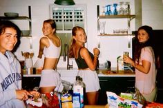 four young women standing in a kitchen with food on the counter and one holding a knife