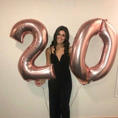 a woman standing in front of a white wall holding two large balloons that spell the number 20