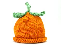 an orange knitted hat with a green ribbon on the brim and two leaves attached to it