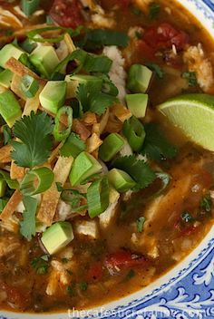 a blue and white bowl filled with chicken tortilla soup topped with avocado