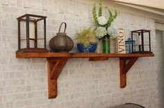 a wooden shelf with vases and other items on it next to a brick wall