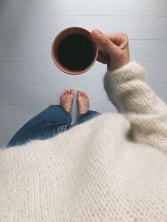 a person holding a cup of coffee while laying on top of a blanket with their feet up