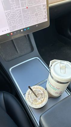 a coffee cup sitting on top of a table next to a laptop computer in a car