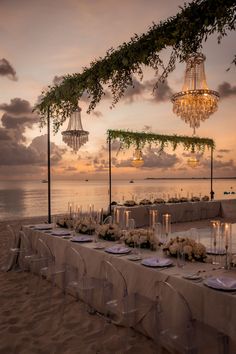 an outdoor dinner setup on the beach with chandeliers hanging from the trees and candles