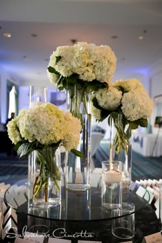 three tall vases filled with white flowers on top of a table