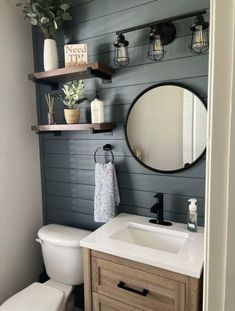 a white toilet sitting under a bathroom mirror next to a wooden sink vanity and shelf