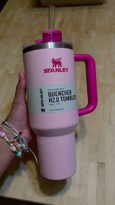 a person holding a pink tumbler on top of a wooden table next to a cup