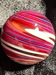 a red and white striped ball sitting on top of a black floor next to a wall