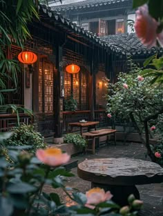 an outdoor area with tables and lanterns in the background, surrounded by plants and flowers