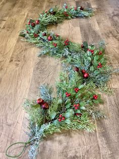 a christmas wreath laying on top of a wooden floor next to other greenery and berries