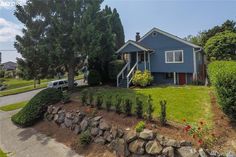 a blue house sitting on top of a lush green hillside next to a tree and shrubbery