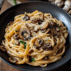 pasta with mushrooms and parmesan cheese in a black bowl on a wooden table