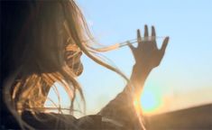 a woman is holding her hand up to the sun