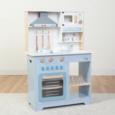 a wooden toy stove and oven with dishes on the top shelf in front of it