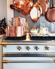 copper pots and pans are hanging on the wall above an oven